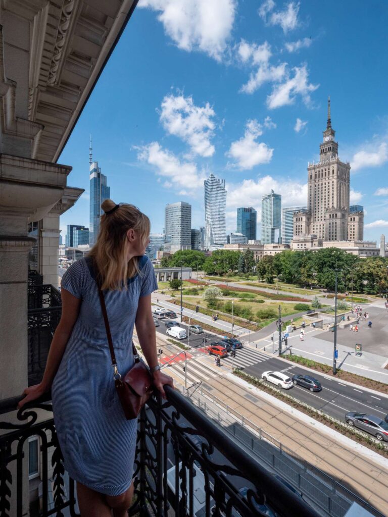 Kobieta oglądająca centrum Warszawy z balkonu w letni pogodny dzień.