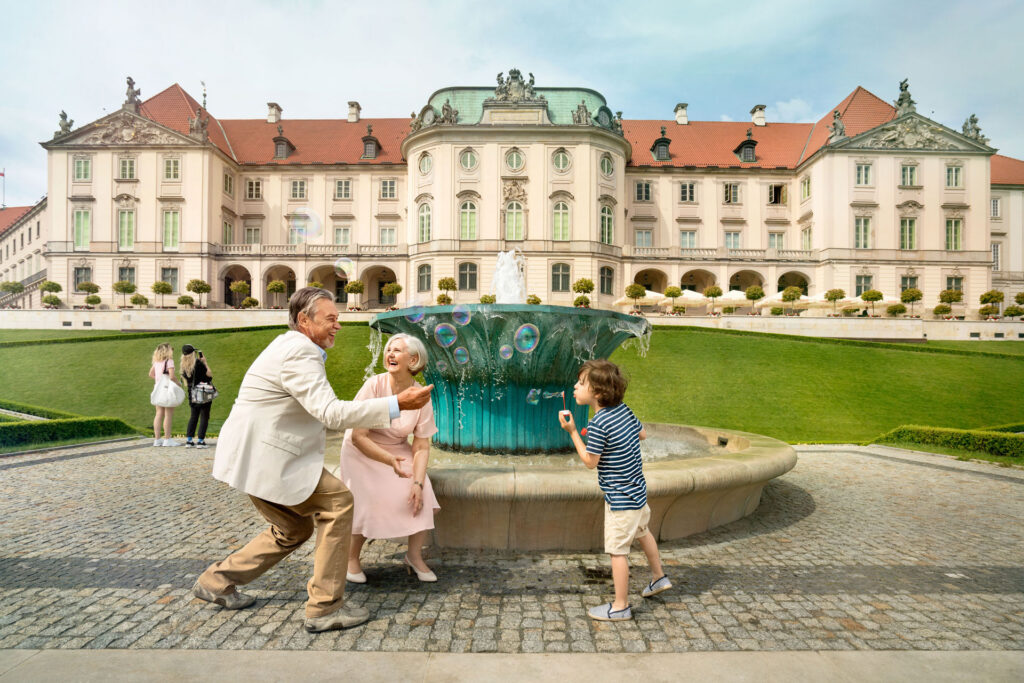Dziecko z dziadkami puszczające bańki przy fontannie na terenie ogrodu Zamku Królewskiego.