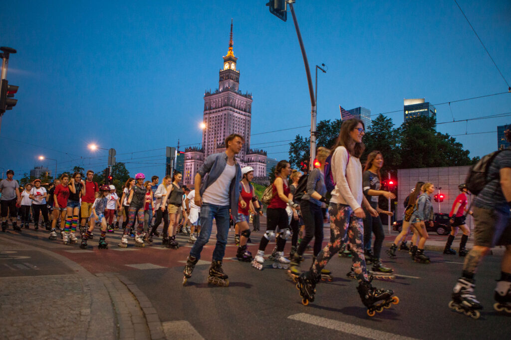 Nocna jazda na rolkach główną ulicą Warszawy. W tle Pałac Kultury i Nauki. Ciepła, letnia noc.