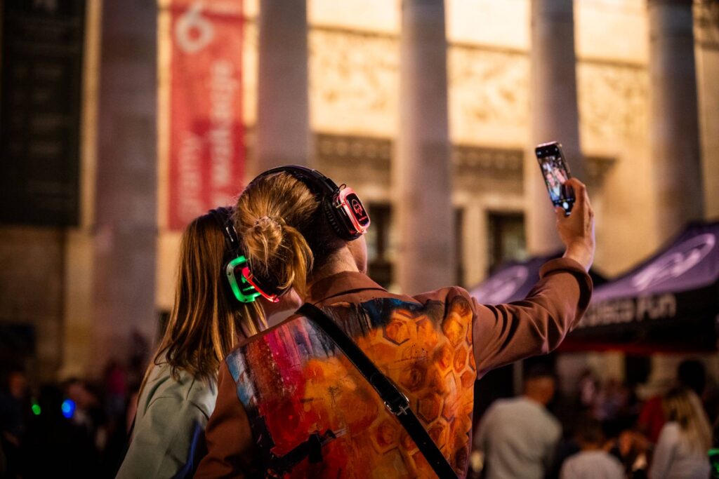 Dwie dziewczyny robią sobie zdjęcie podczas nocnego silent disco. W tle kolumny Pałacu Kultury.