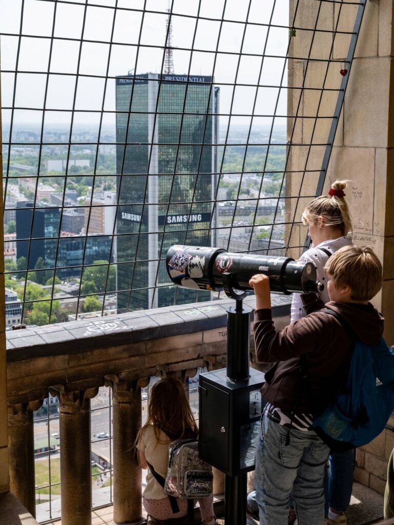 Grupa dzieci przygląda się panoramie miasta przez lunetę